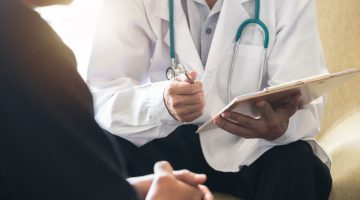 doctor wearing a white coat and stethoscope holding a clipboard