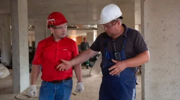 two men conversing on a construction site, wearing proper personal protective equipment