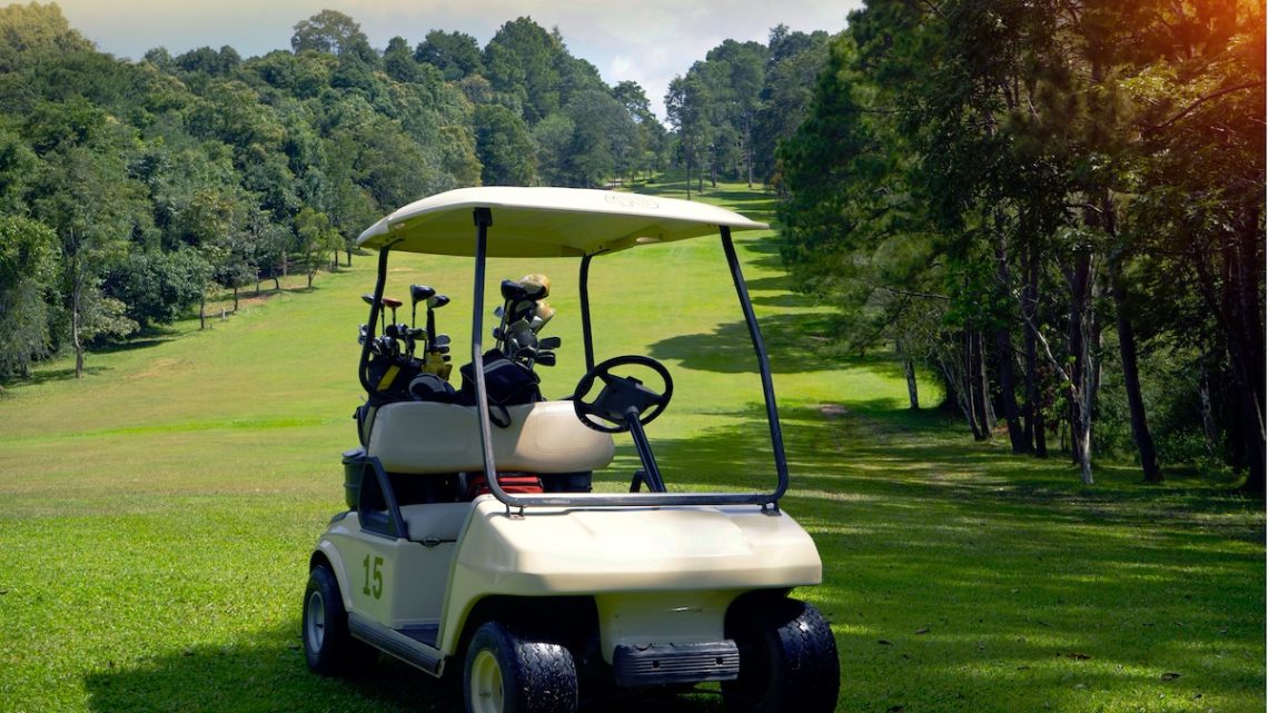 Golf cart parked on a golf course fairway surrounded by trees.
